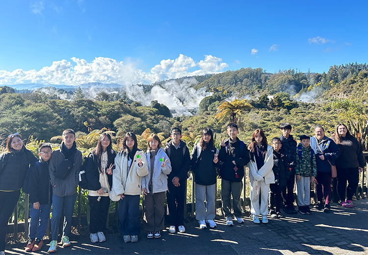 同學在溫泉地熱區散步拍照,身後山林間升起蒸氣雲霧,呈現壯麗的自然奇景 | 新西蘭遊學團